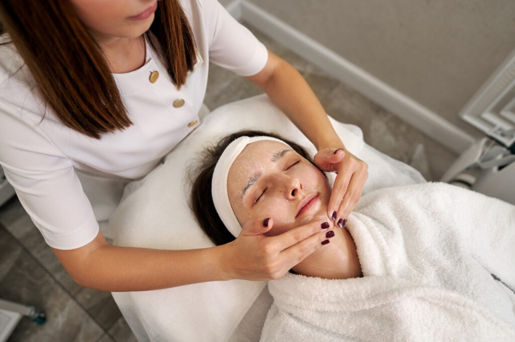 A person is receiving a facial treatment from an esthetician in a peaceful spa setting, with a focus on relaxation and skincare.