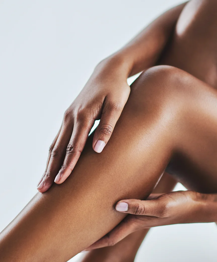 The image shows a close-up of a person's hand gently touching their own smooth leg, suggesting themes of skin care or body positivity. The background is neutral and minimalist.