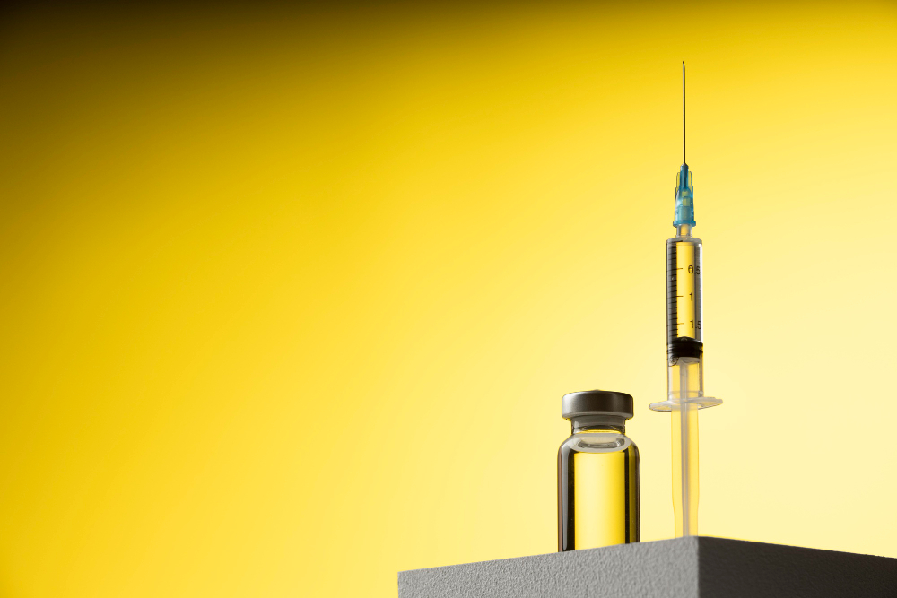 An upright syringe with a needle is poised next to a small vial on a gray surface, set against a gradient yellow background.