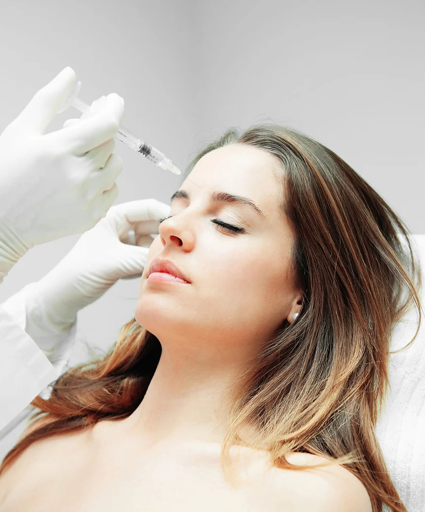 A person is receiving an injection near the forehead, administered by a gloved hand, suggesting a medical or cosmetic procedure in a clinical setting.