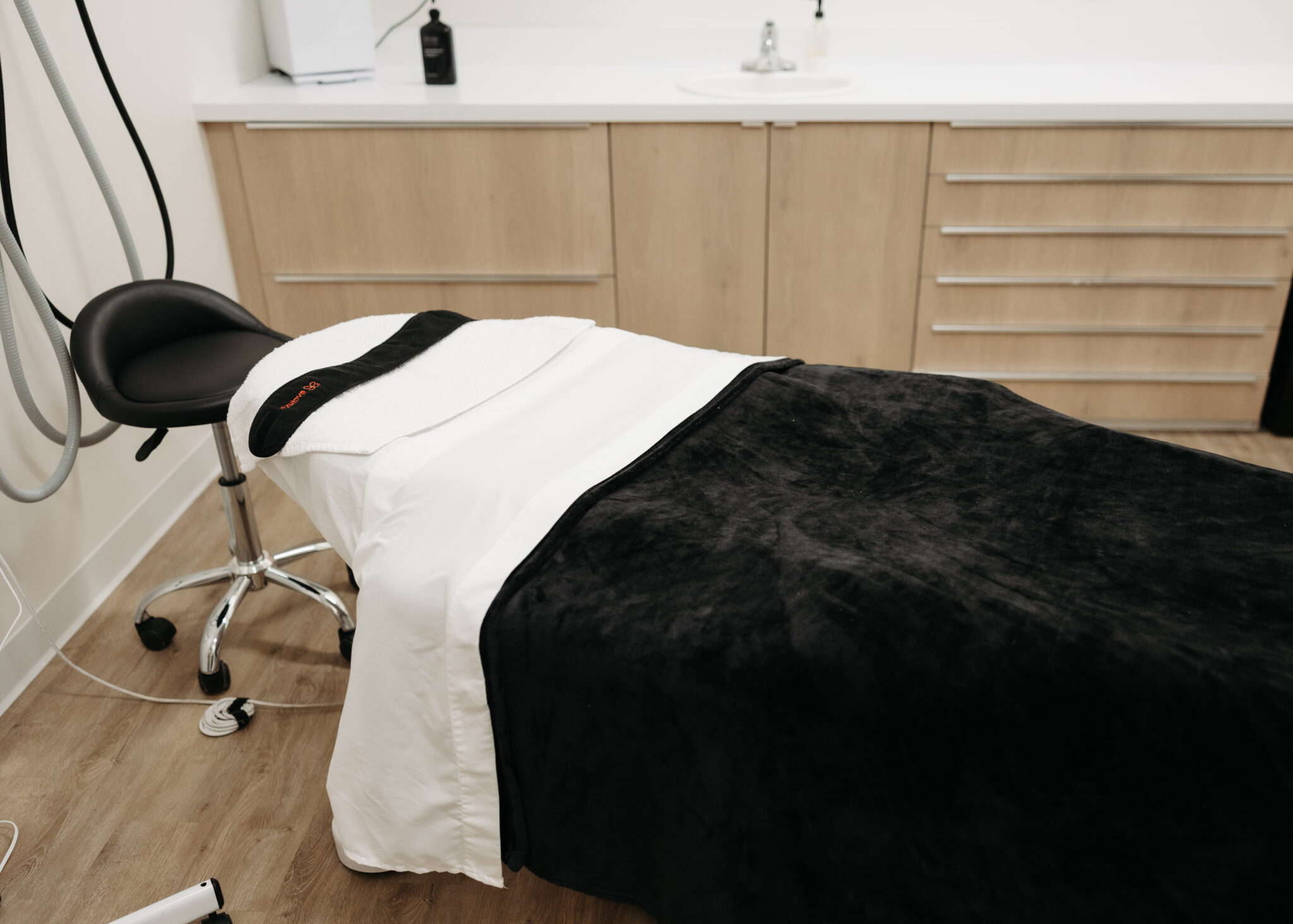 A treatment room with a massage table, stool, and cabinets. The neutral tones create a calm, professional atmosphere.