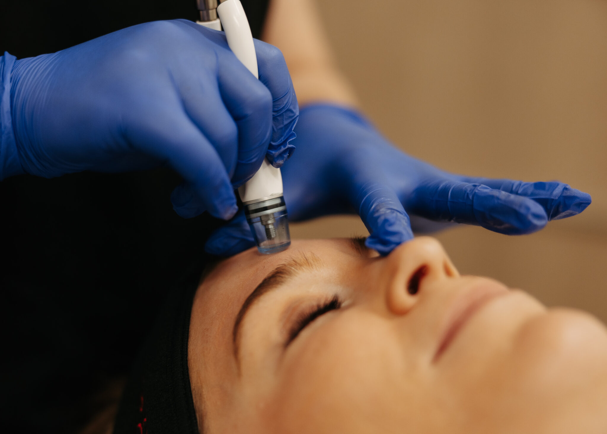 A person is receiving a facial treatment using a specialized tool, performed by someone wearing blue gloves.