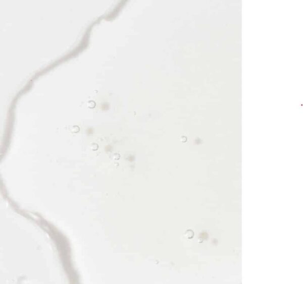 The image depicts a close-up of a white liquid, possibly milk, with a visible spill or splash pattern and droplets against a white background.
