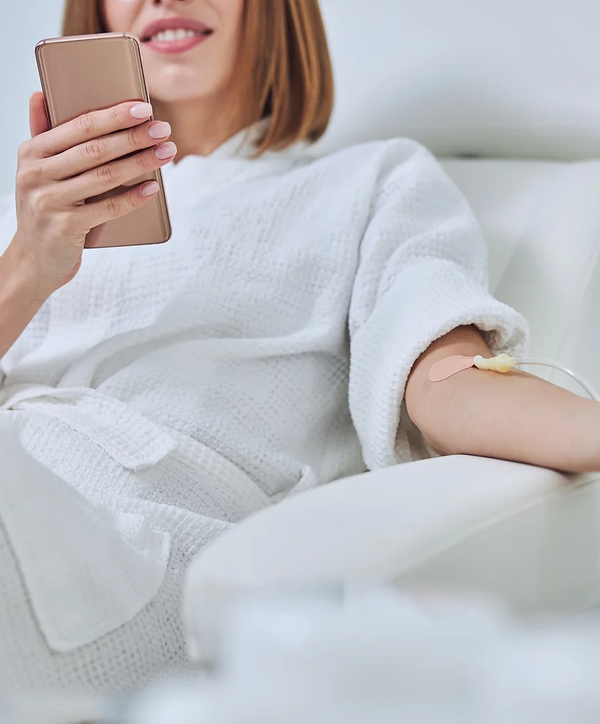 A person is reclining, holding a phone, with a bandage on their arm, possibly after a medical procedure like blood donation or vaccination.