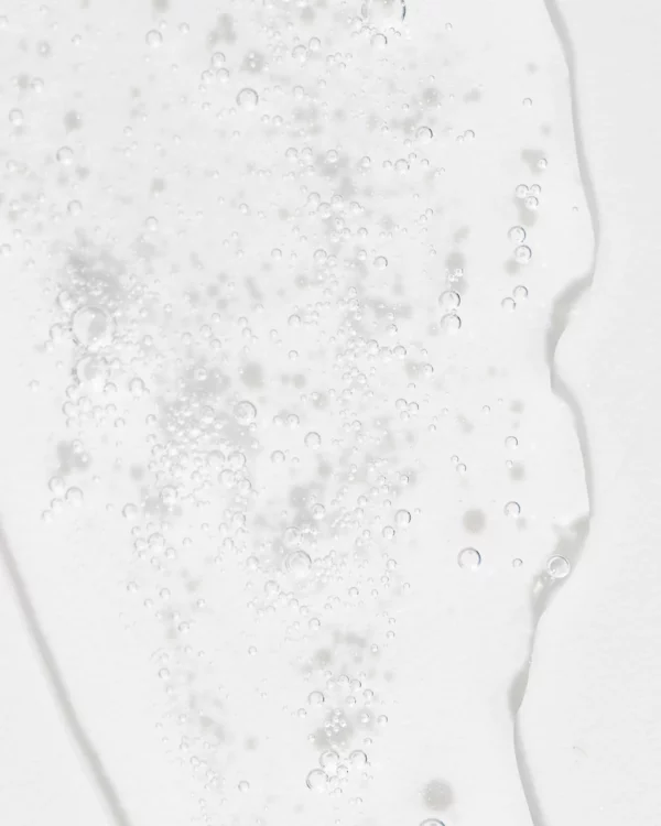 The image displays a close-up of transparent bubbles of various sizes on a white, wet surface, creating an abstract and textural appearance.