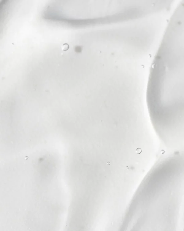 This image shows a close-up view of a creamy, viscous substance with small air bubbles. It is a homogenous and smooth texture with slight shadows.