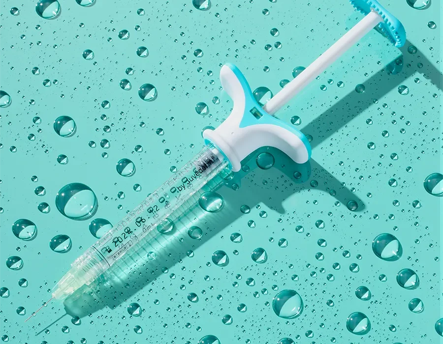 A medical syringe with a blue handle lies on a teal surface dotted with water droplets, suggesting cleanliness or medical hygiene.