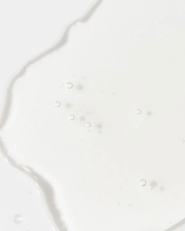 The image depicts a white, creamy liquid with a smooth texture and tiny air bubbles, possibly milk, spilling over a plain surface.