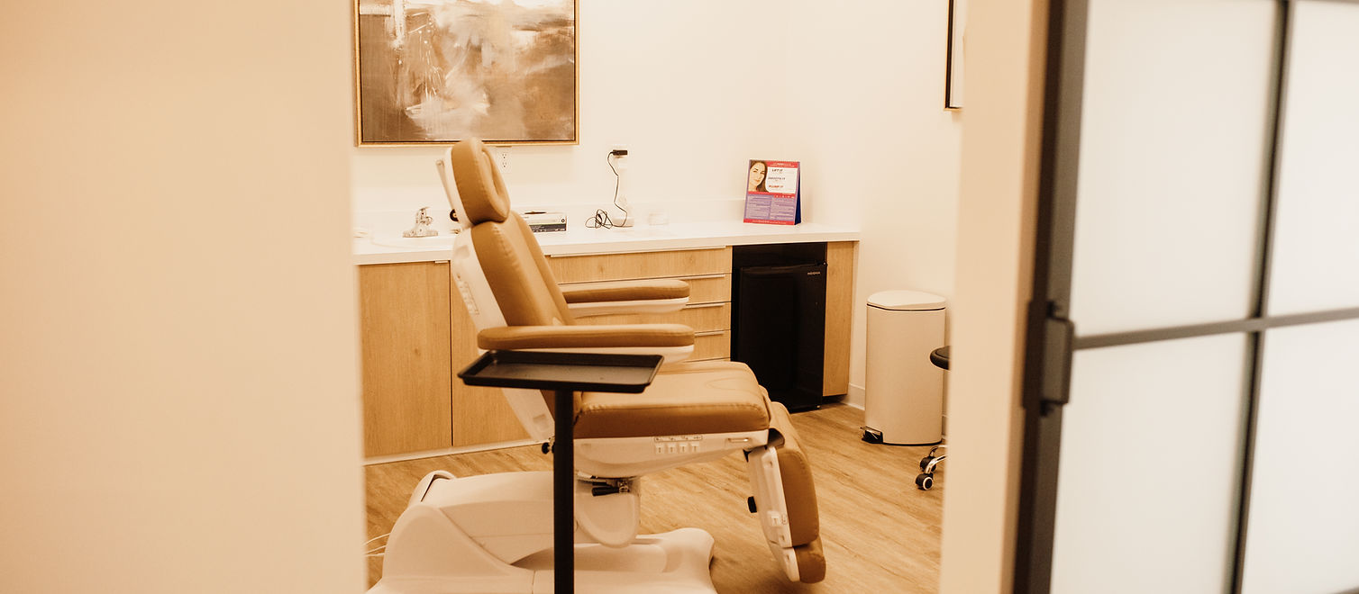A clean, modern dental office with a beige patient chair, cabinetry, a small trash bin, and framed abstract artwork on the wall.