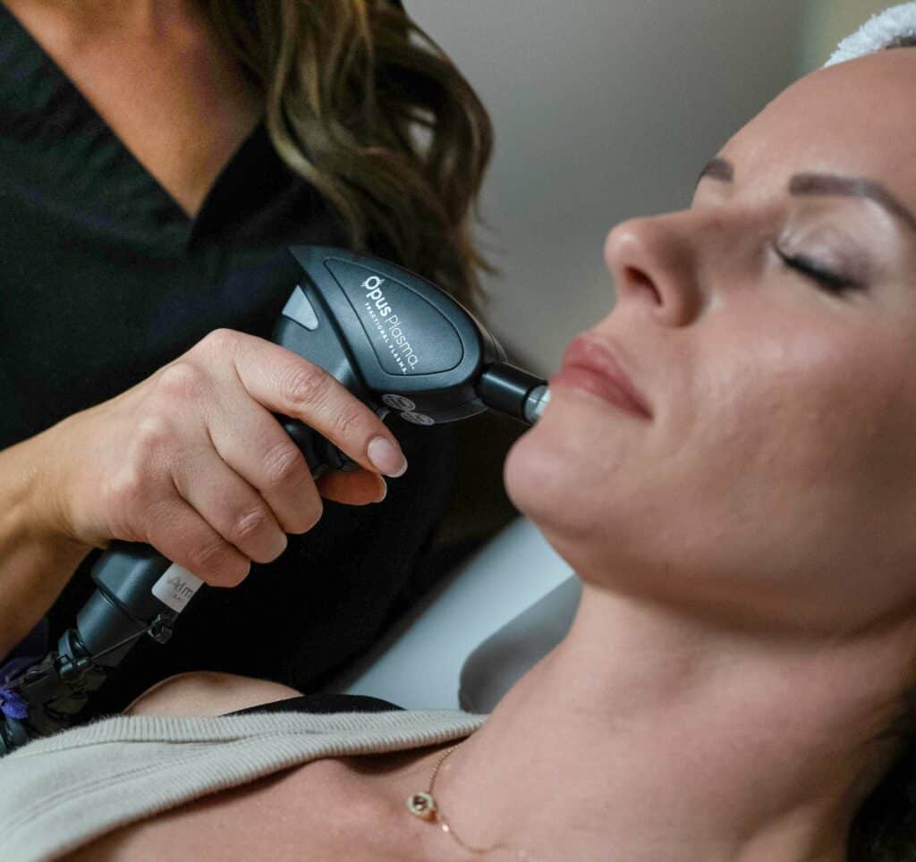 In the image, a person is performing a skin treatment on another person's face using a handheld medical device. The recipient appears relaxed.