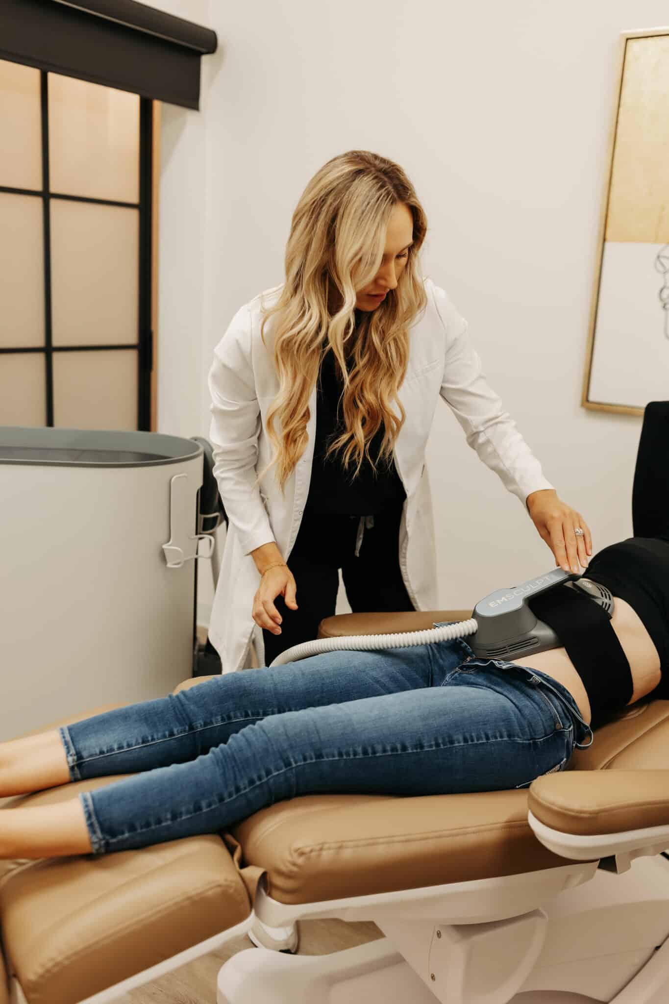 A healthcare professional in a white coat examines a patient lying on a medical bed with a device attached to their abdomen.