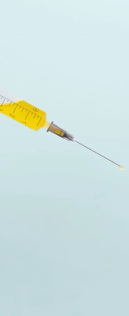 An isolated syringe with a yellow plunger and clear barrel containing a liquid is depicted against a plain light background, with a needle extending outwards.