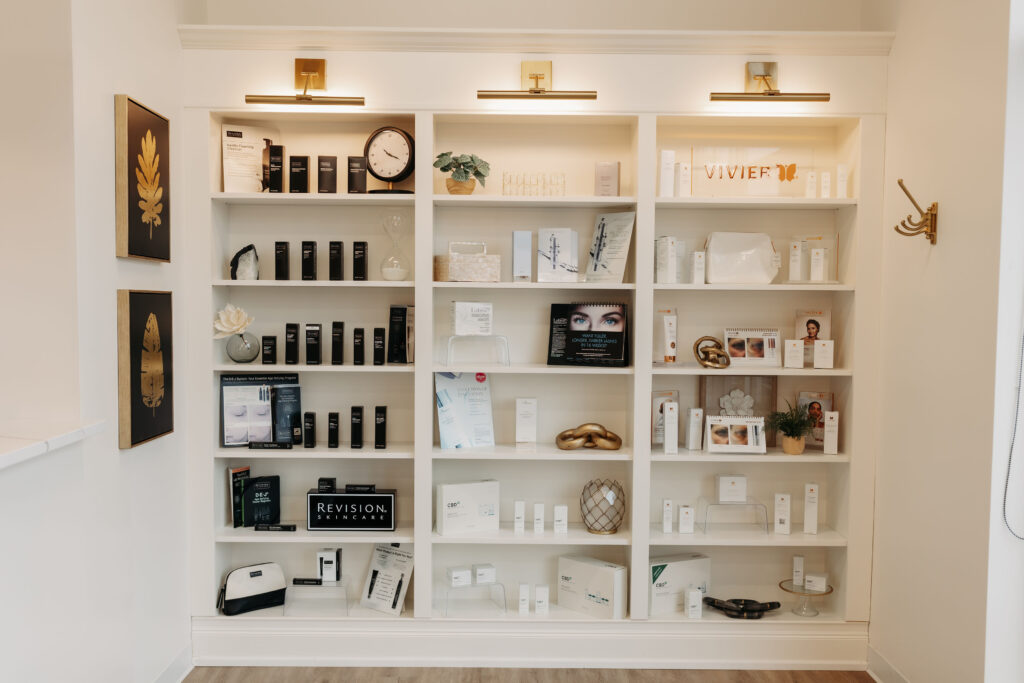 A well-lit display shelf showcases various skincare products, promotional material, a clock, and decorative items in a minimalist, contemporary setting.