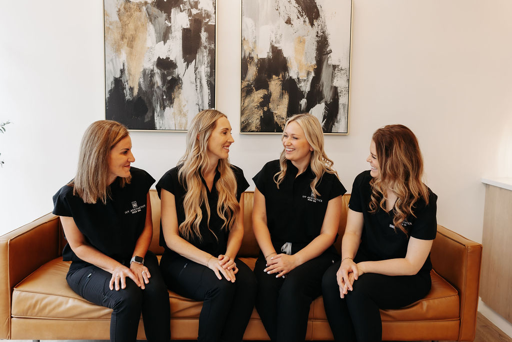 Four seated people in black uniforms on a tan couch, with abstract paintings on the wall behind them.