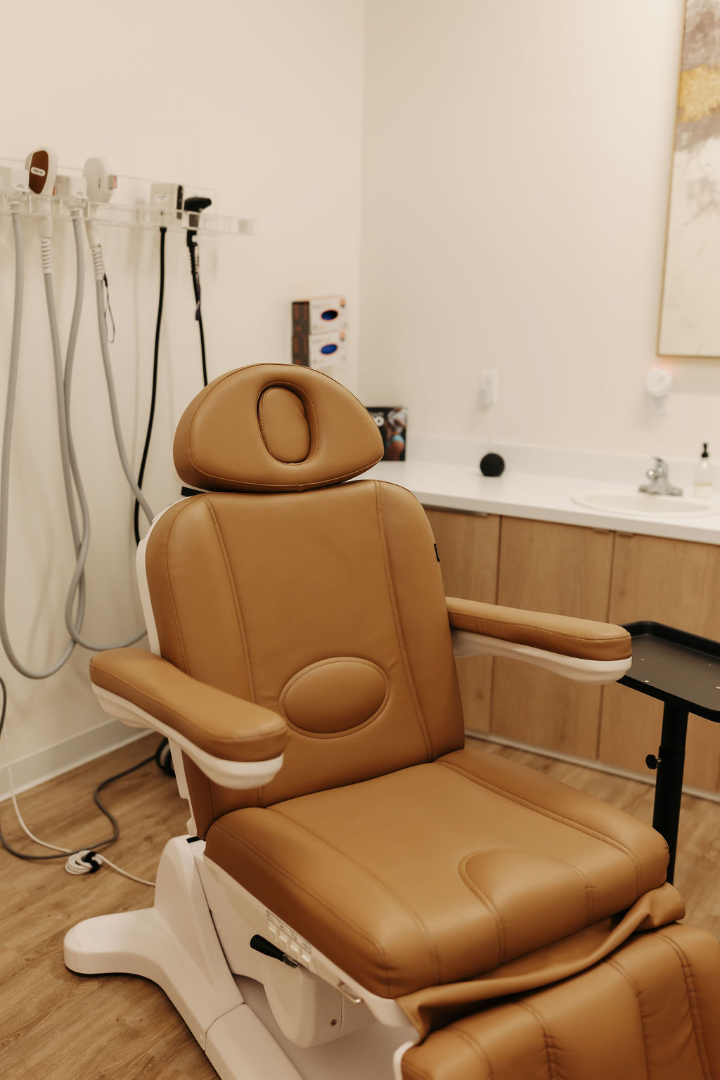 A spa or medical office features a brown recliner chair, equipment, sink, and neutral decor, suggesting a clean, professional environment.