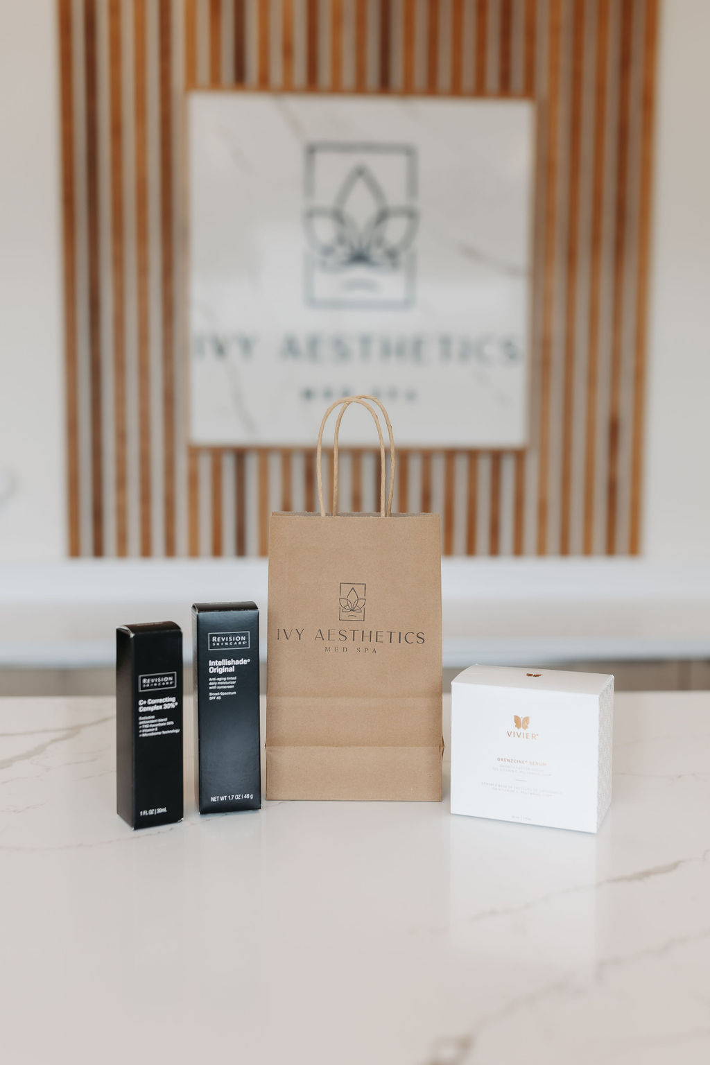 Skincare products from Ivy Aesthetics Med Spa on a marble table, with branded gift bag in focus, against a modern wooden backdrop.