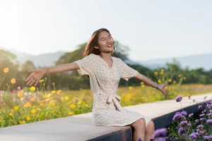 A person sits joyfully on a bench, arms outstretched, surrounded by a colorful field of wildflowers under a clear sky.