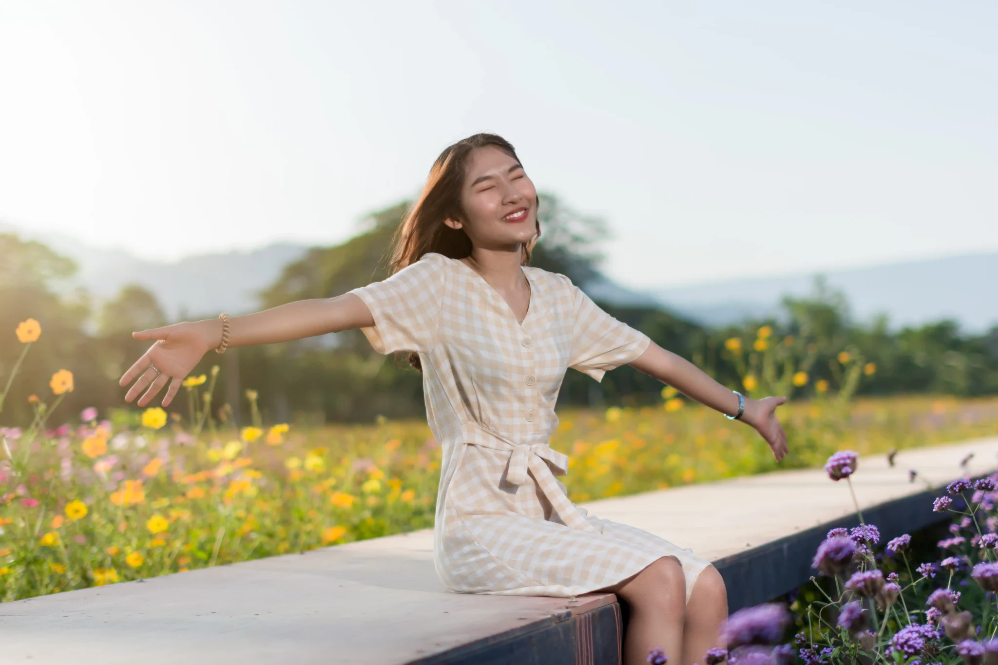 A person sits joyfully on a bench, arms outstretched, surrounded by a colorful field of wildflowers under a clear sky.