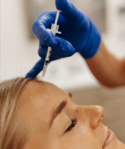 A person receives a cosmetic injection in the forehead. A gloved hand holds the syringe, highlighting a clinical setting.