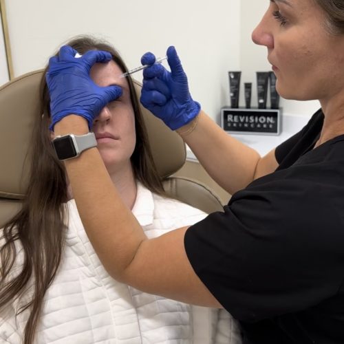 A person in blue gloves is examining another person's eye who is reclining and has their eyes closed, possibly during a medical or cosmetic procedure.