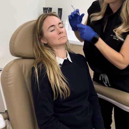 In a clinical setting, a person wearing gloves appears to be preparing to administer a treatment to a relaxed individual seated in a chair.