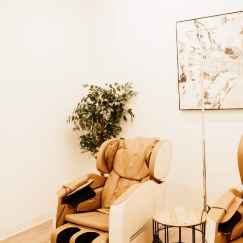 This is a tranquil room with a beige massage chair, a green potted plant, a framed abstract artwork, and a minimalist side table.